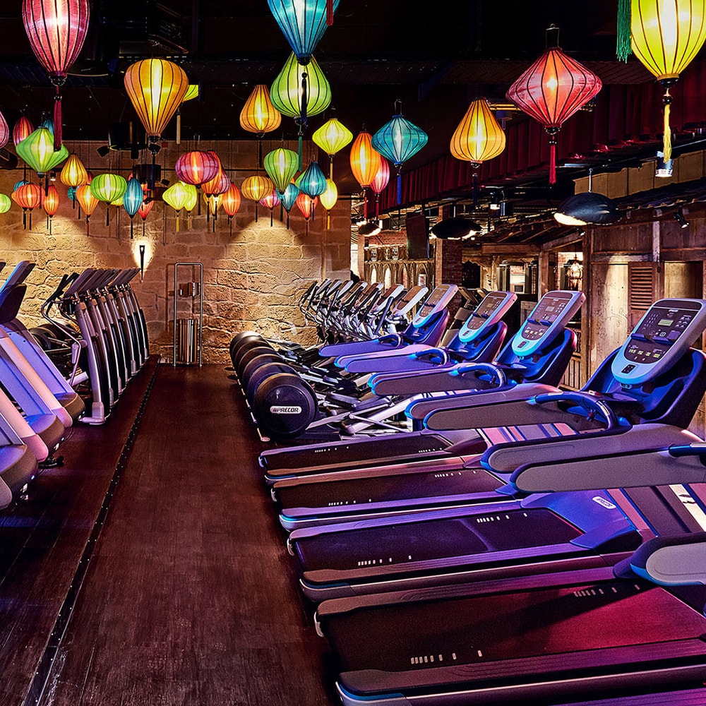 Rows of Treadmills in the interior of a McFit location underneath an arrangement of blue, green, orange and red paper lanterns.