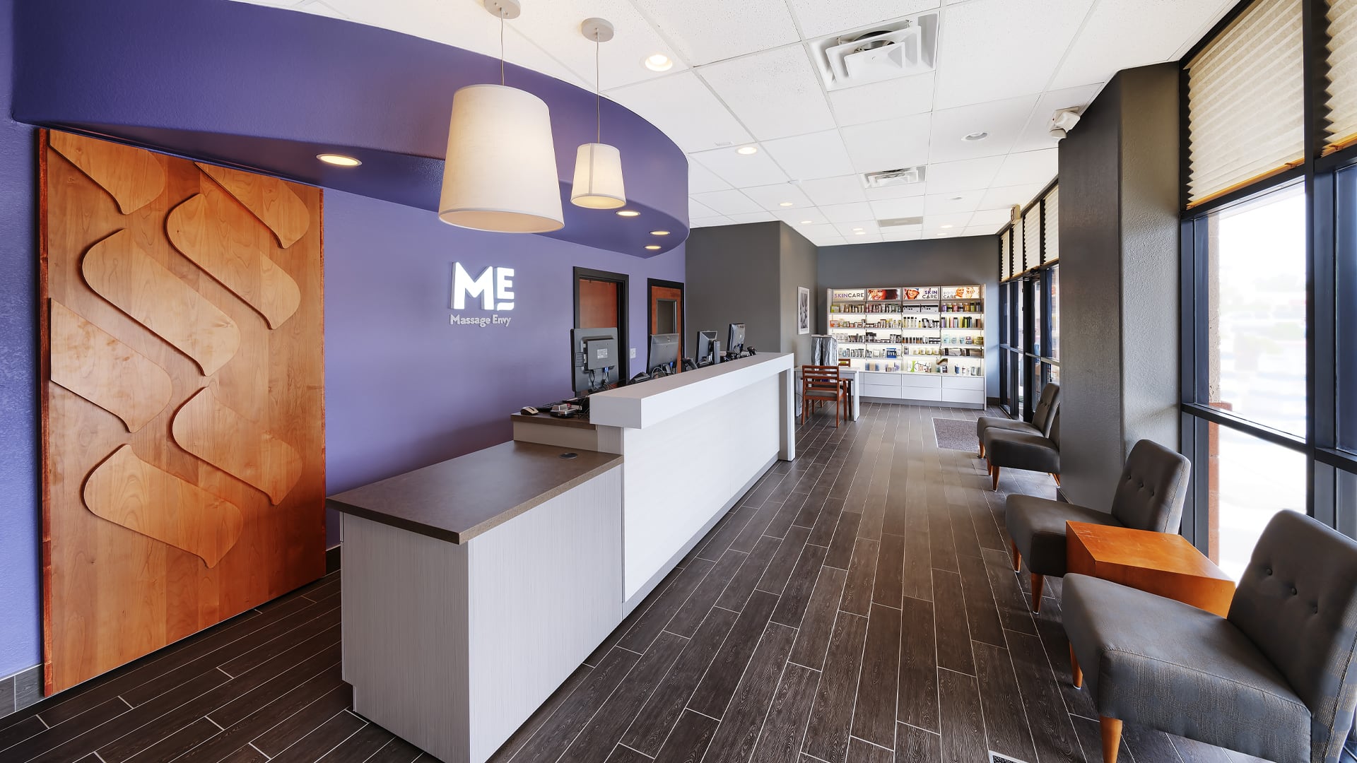 Inside a Massage Envy location with Purple walls and exposed wood and plus chairs in the waiting area.