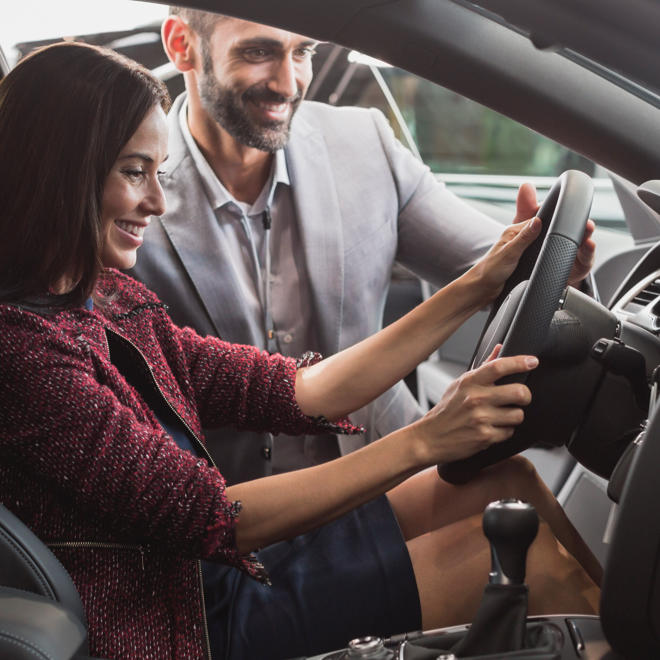 An Enterprise Holding's employee standing over a customer who's seated in the driver's seat of a new car.