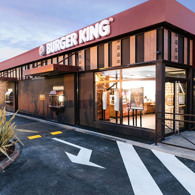 Outside a Burger King Location with large windows and Burger King in large white letters lines the top of the building.